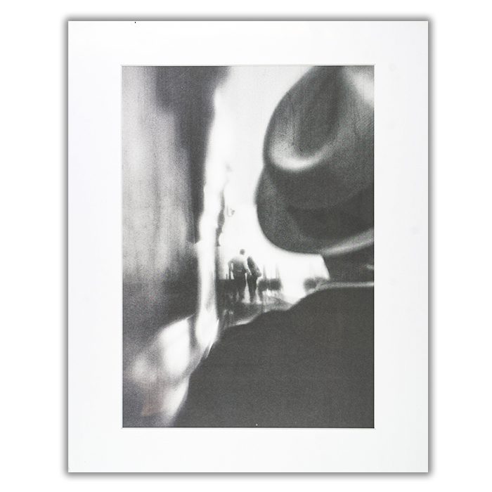 Gone Are The Days Fotograf: Laura Mexia En suddig svartvit bild av en man i hatt i förgrunden och ett par som omfamnar varandra i bakgrunden
